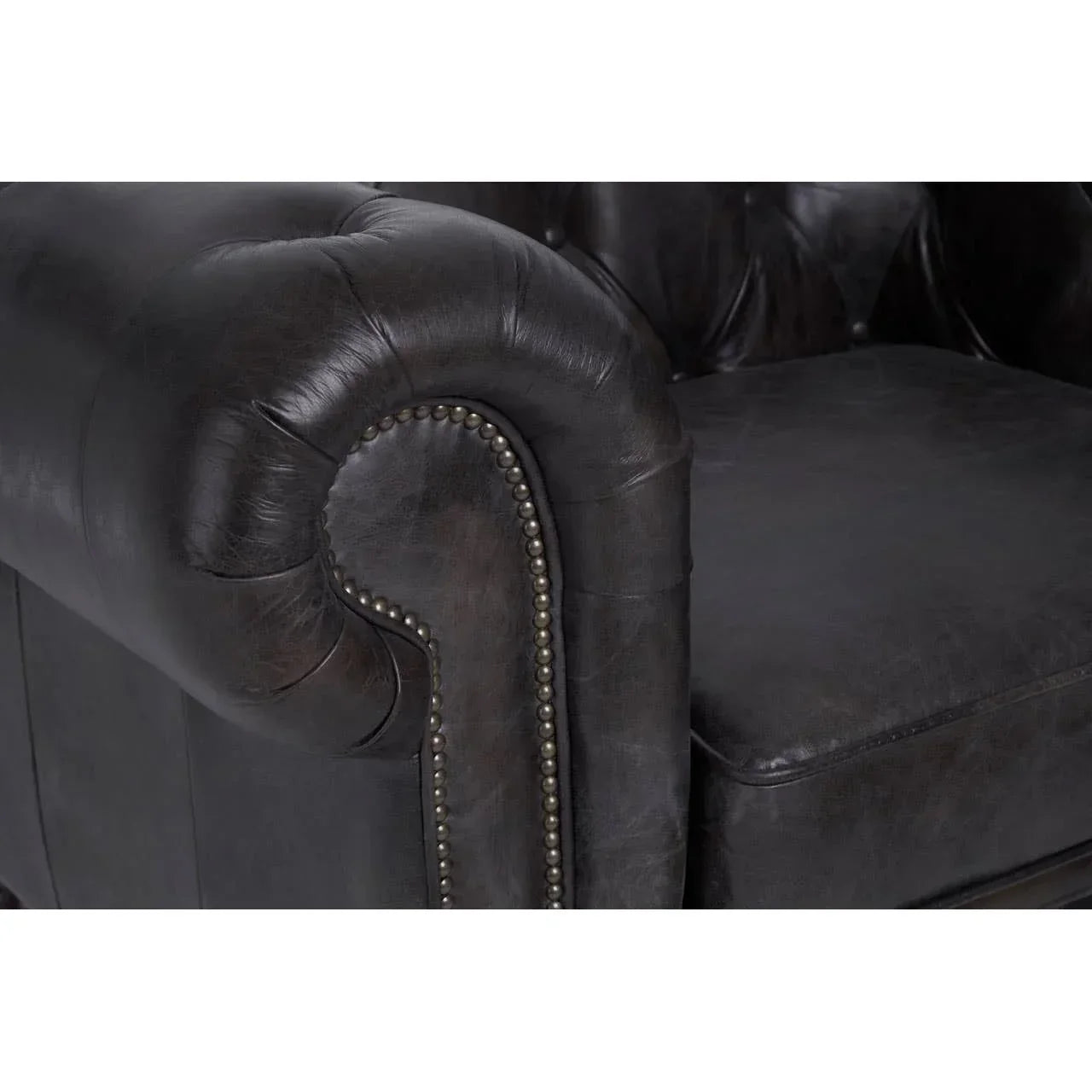 Close-up of dark leather sofa arm with button tufting and decorative metal stud detail