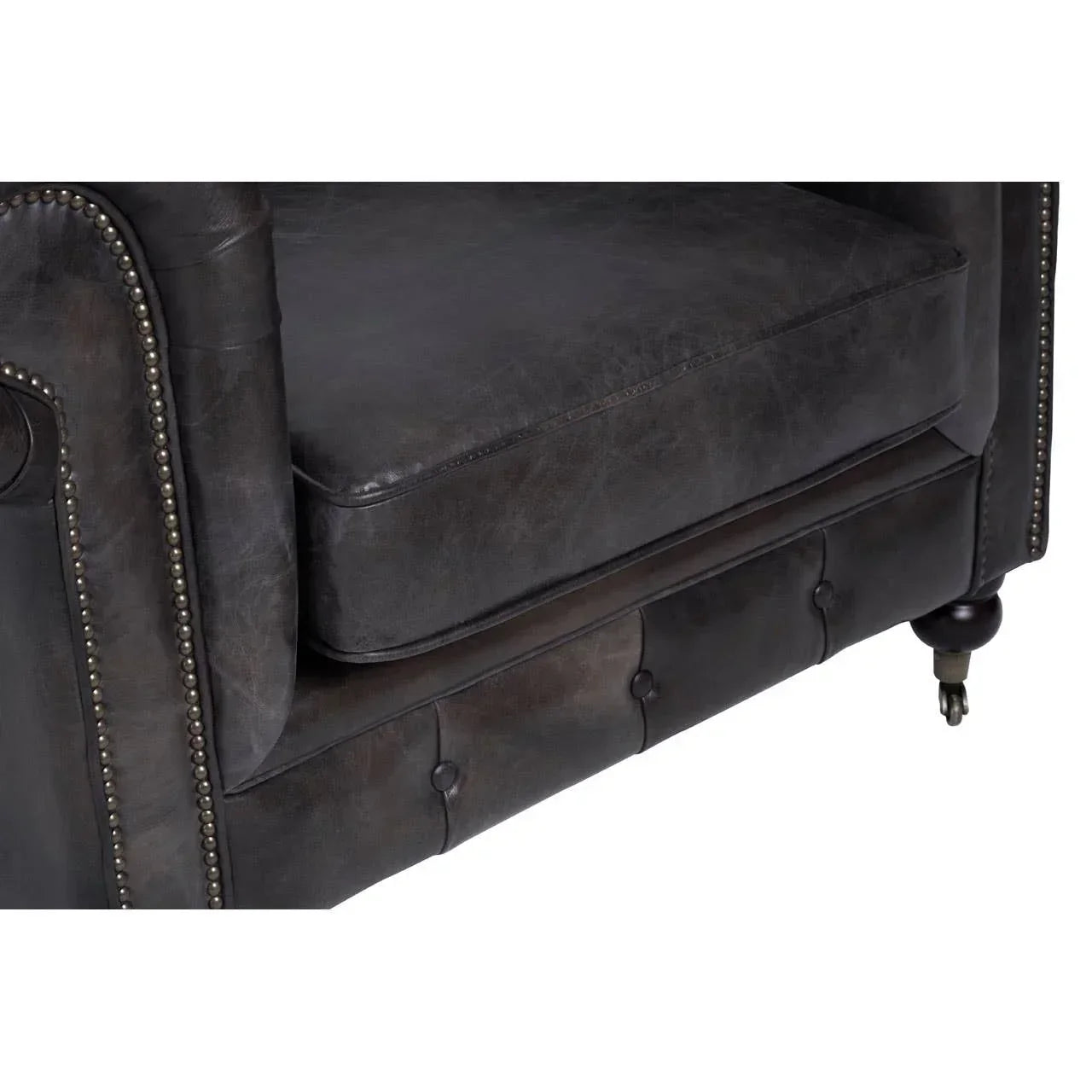 Dark leather sofa corner with studded armrest and turned wooden leg on castor