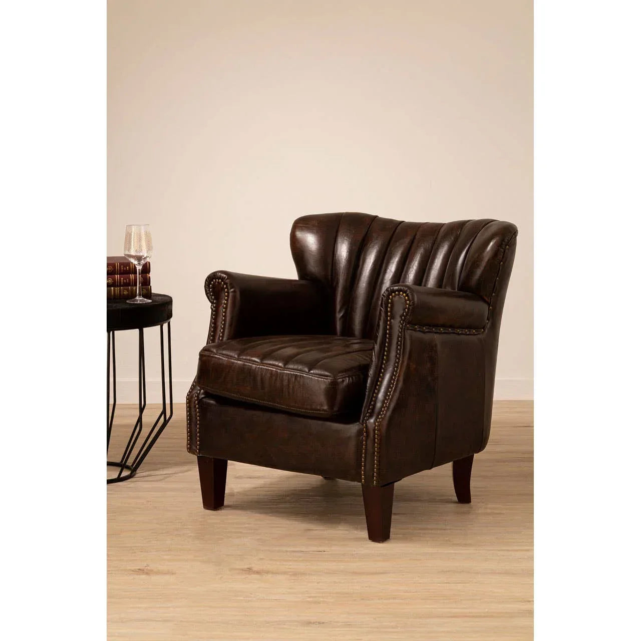 Dark brown leather armchair with studded arms and cushion, set on light wood flooring