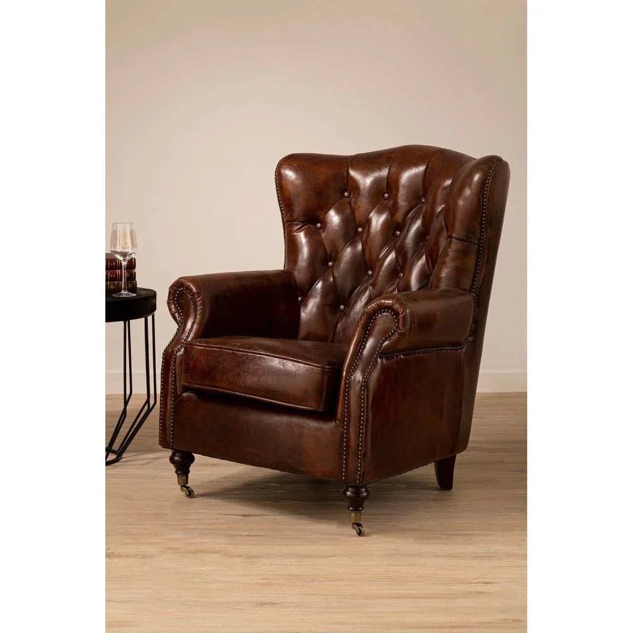 Brown leather armchair with button-tufted back and brass nailhead trim on wooden floor