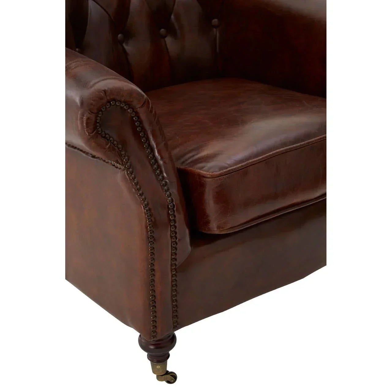 Closeup of brown leather sofa arm with button tufting and brass stud detail