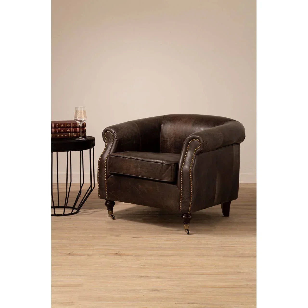 Dark brown leather armchair with brass stud detailing beside a wooden side table on oak flooring