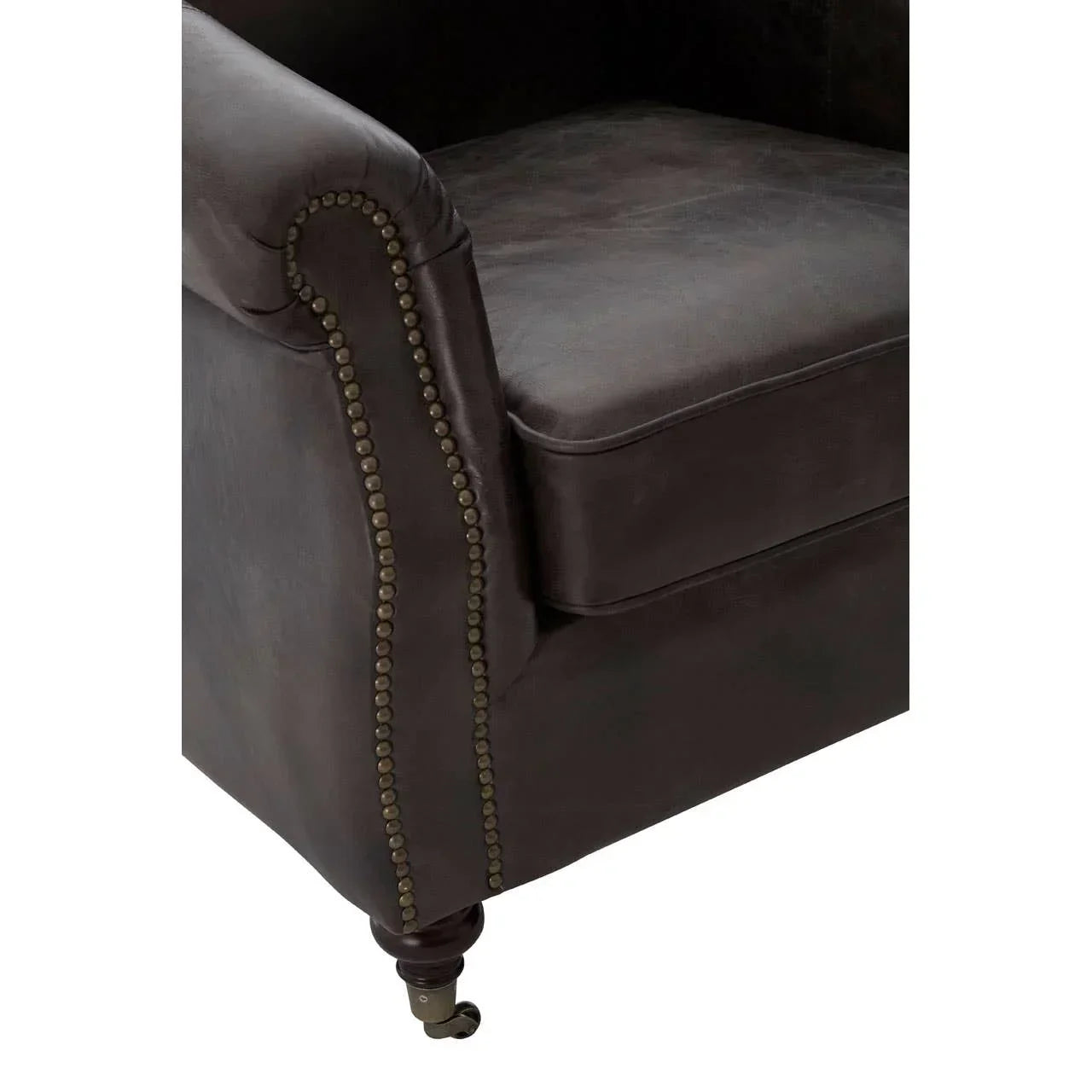 Close-up of dark brown leather armchair with brass stud detailing and wooden castor leg