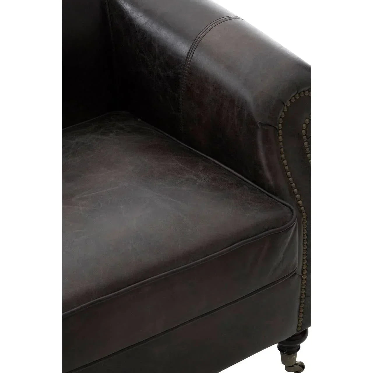 Close-up of dark brown leather armchair with brass stud detail and wooden sofa leg