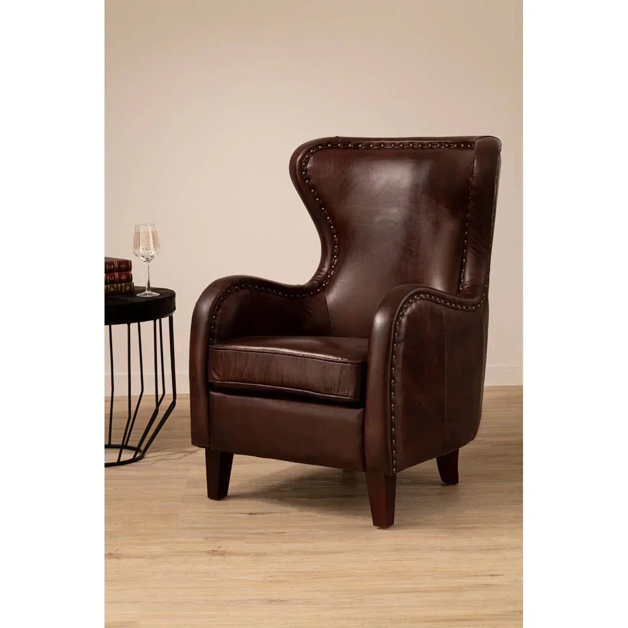 Brown leather accent armchair with nailhead trim and wooden legs beside round black side table