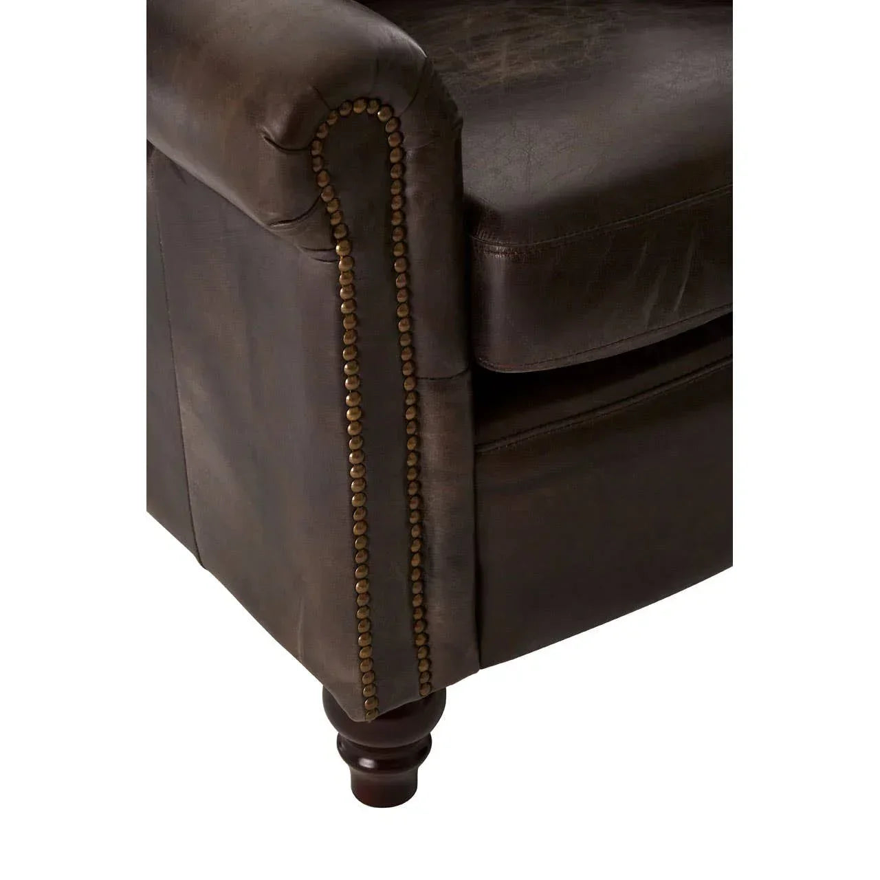 Close up of brown leather sofa arm with brass nailhead trim and wooden leg