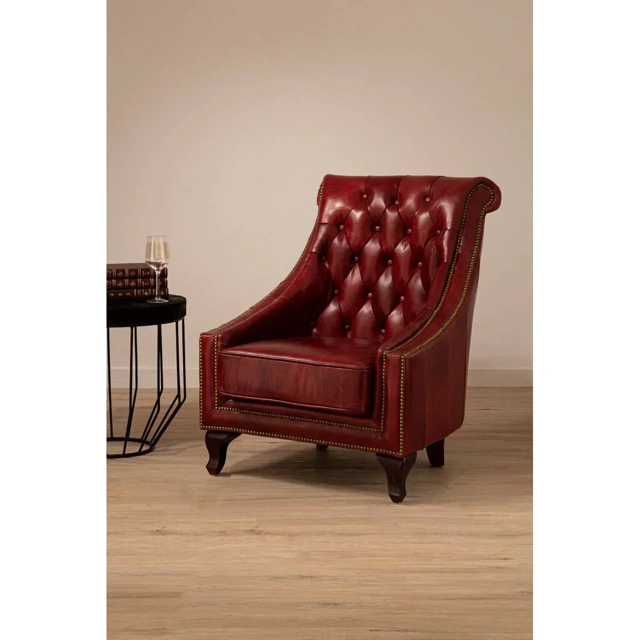 Red leather armchair with button-tufted back and brass stud trim on wooden floor