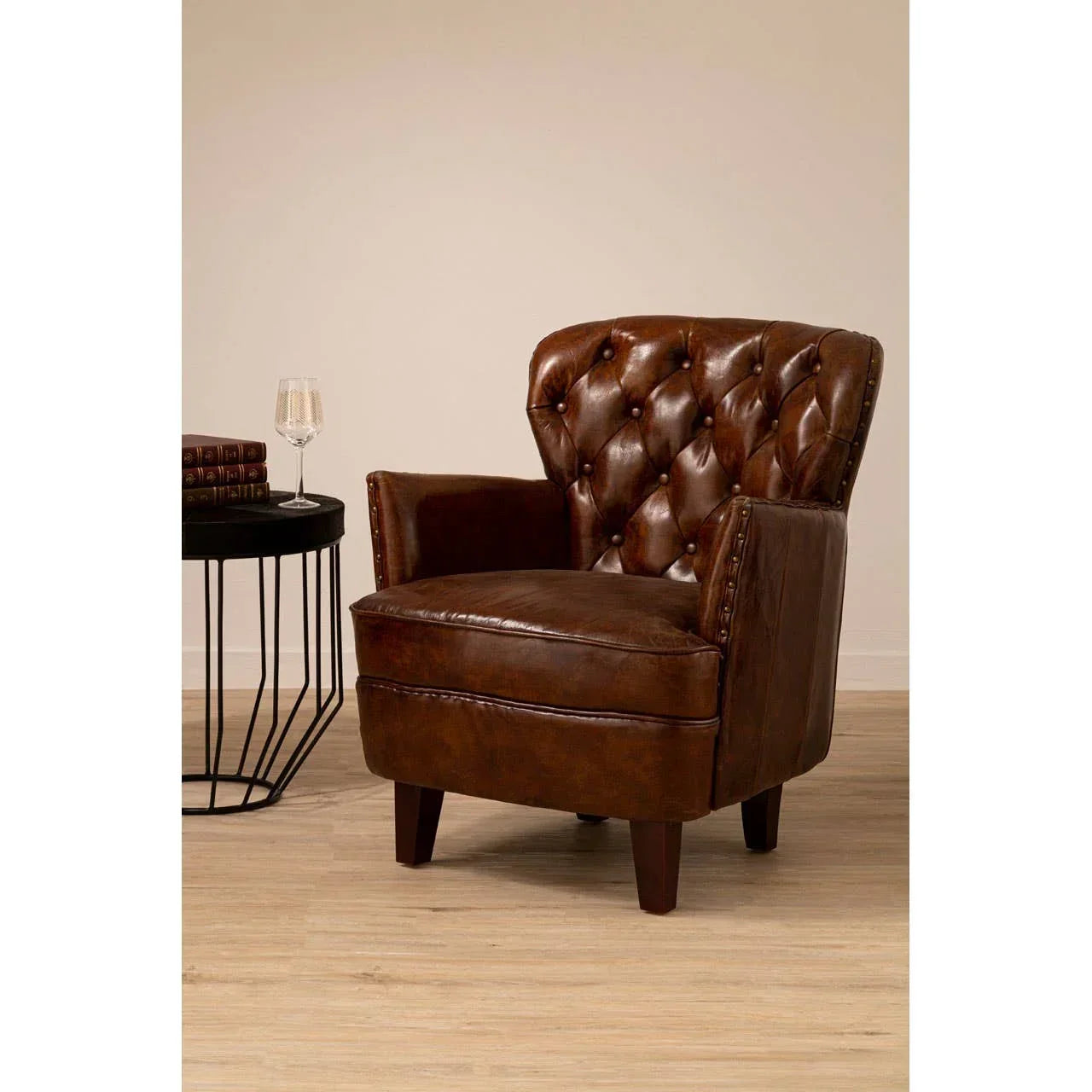 Brown leather armchair with button tufted backrest and wooden legs on light wood floor
