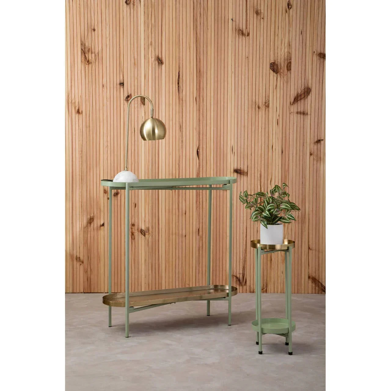 Green metal console table with brass shelf and lamp beside matching plant stand against wood panel wall