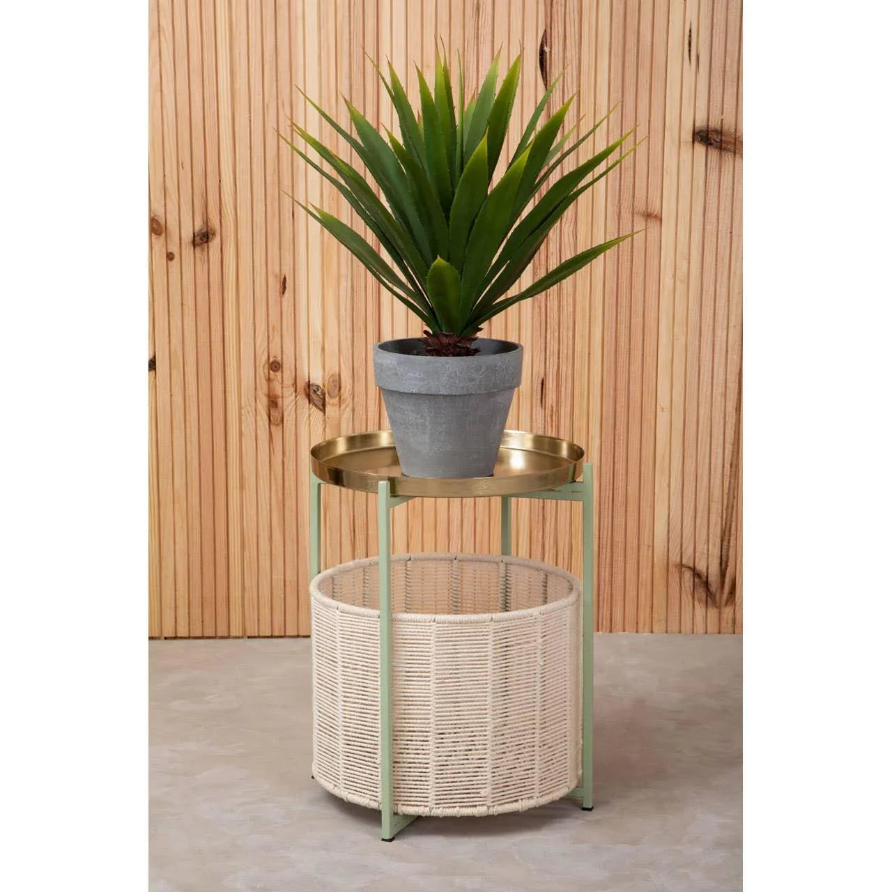 Round rattan side table with gold tray top and potted plant against wood panel wall