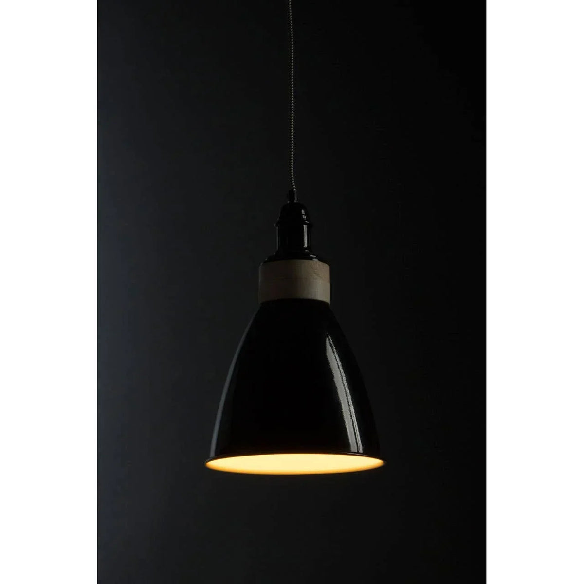Black pendant light with wooden accent and warm glow against dark background