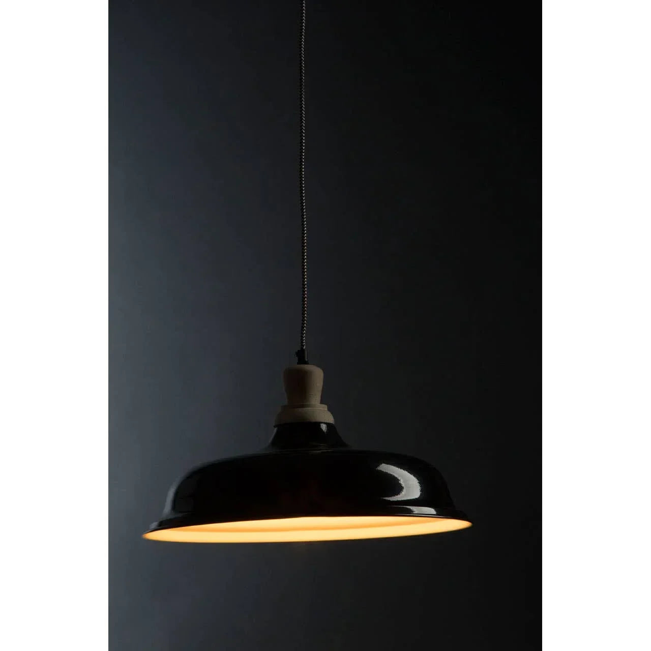Black metal pendant light with wooden fixture and warm glow hanging against dark background