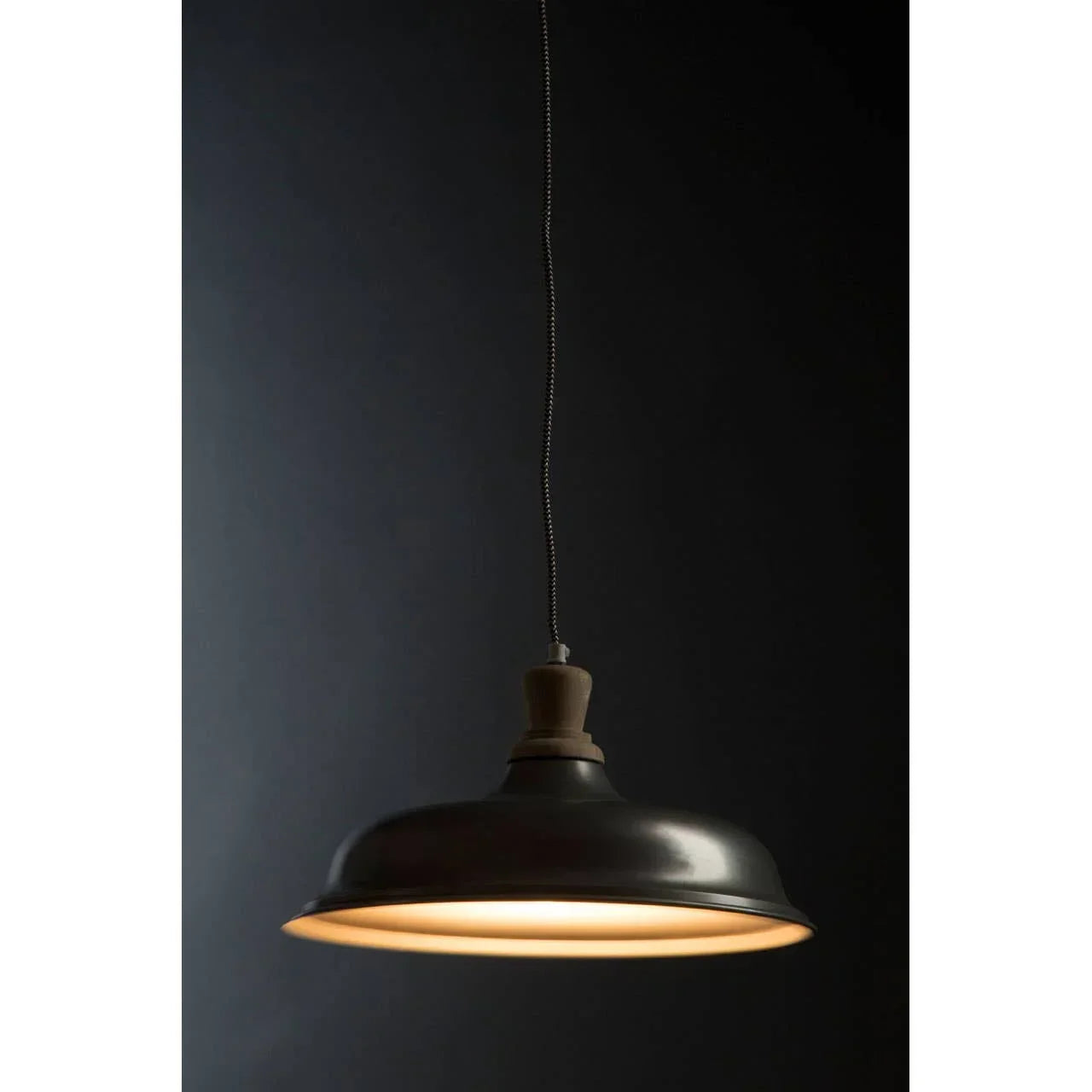 Black metal pendant light with wooden top and warm glow against dark background