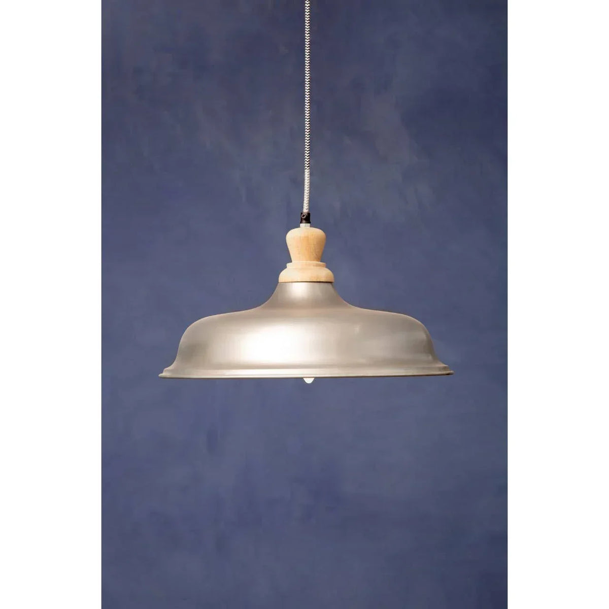 Metal pendant ceiling light with wooden top and fabric cord against blue background