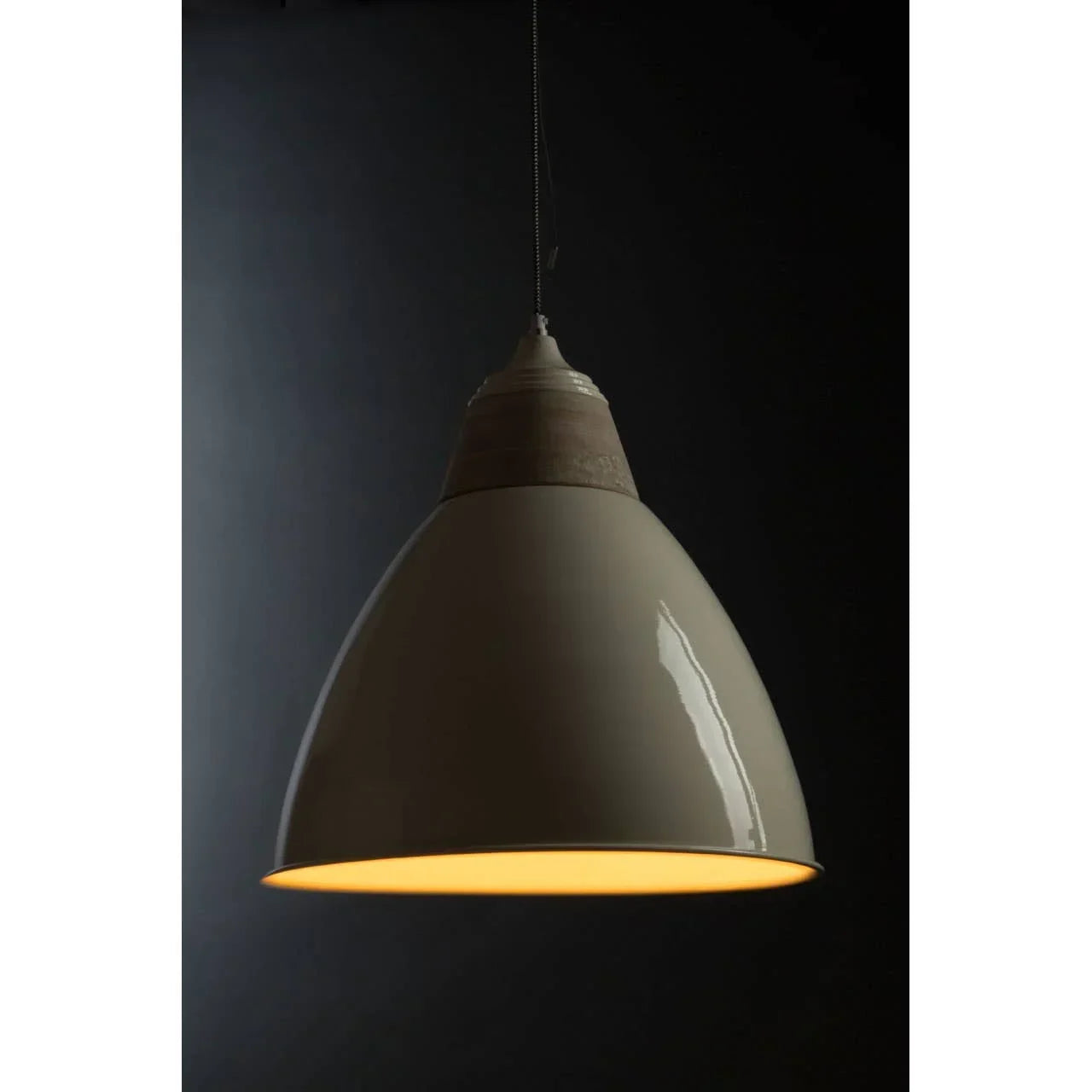 Beige metal pendant light with wooden top detail, lit in a dark interior setting