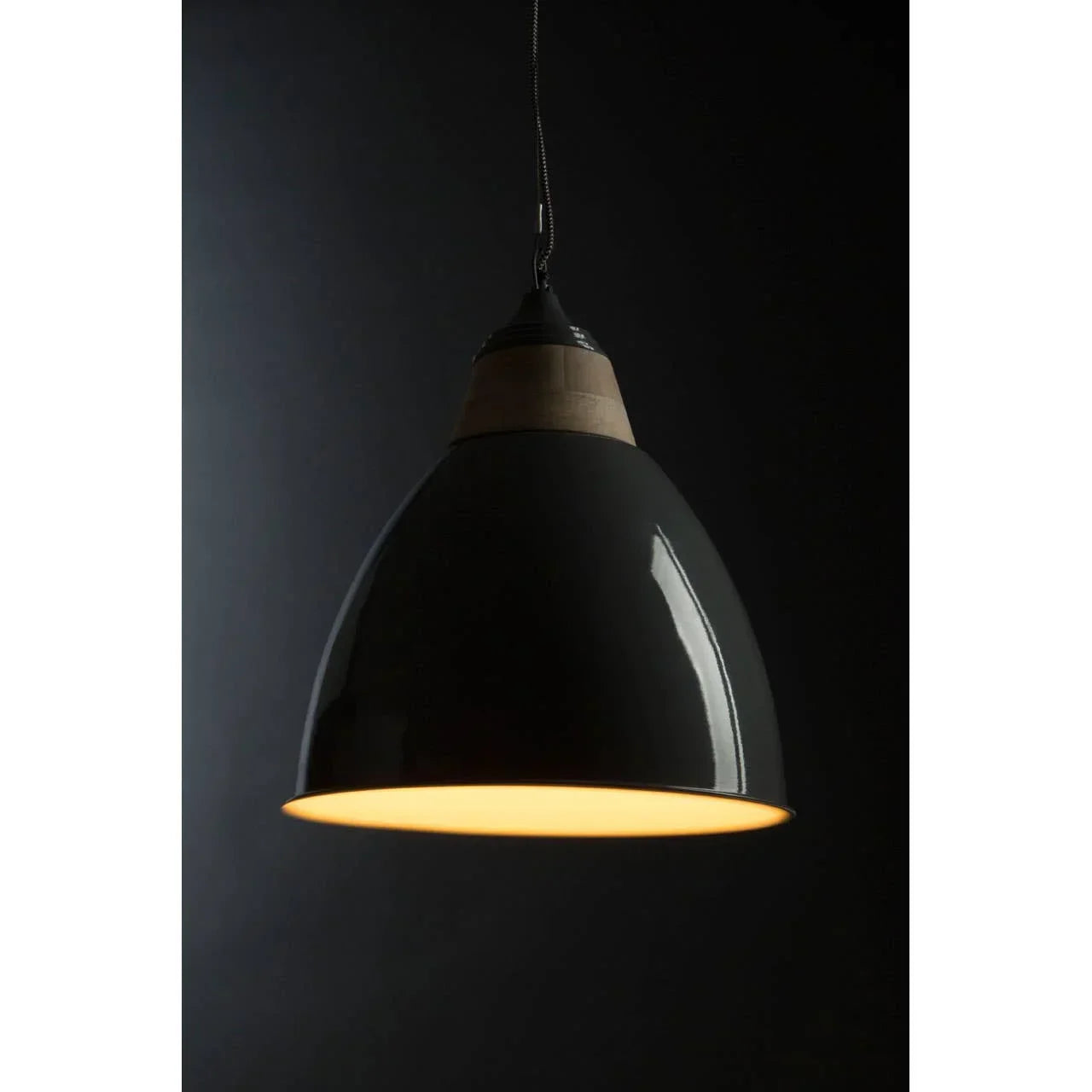 Black metal pendant ceiling light with wood detail, illuminated against dark background