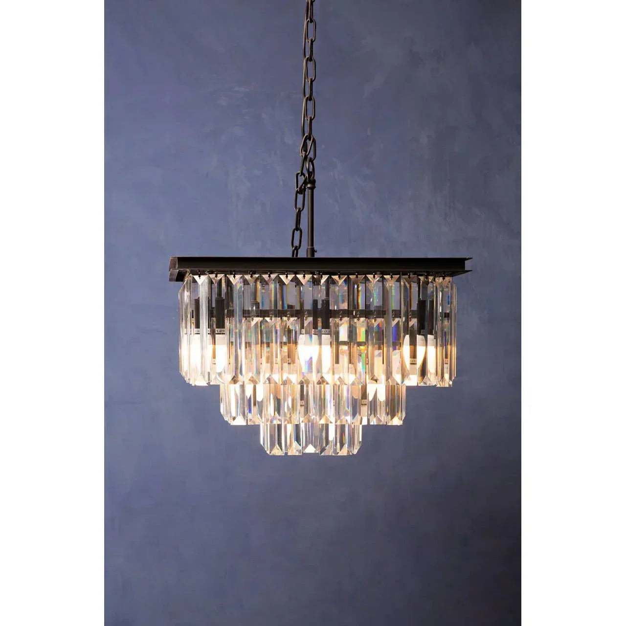 Rectangular crystal chandelier with tiered glass prisms and black chain against blue wall