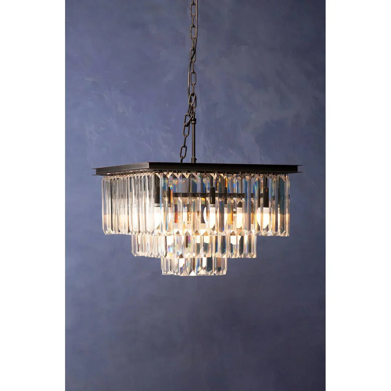 Square crystal chandelier with tiered glass prisms and metal chain against blue wall
