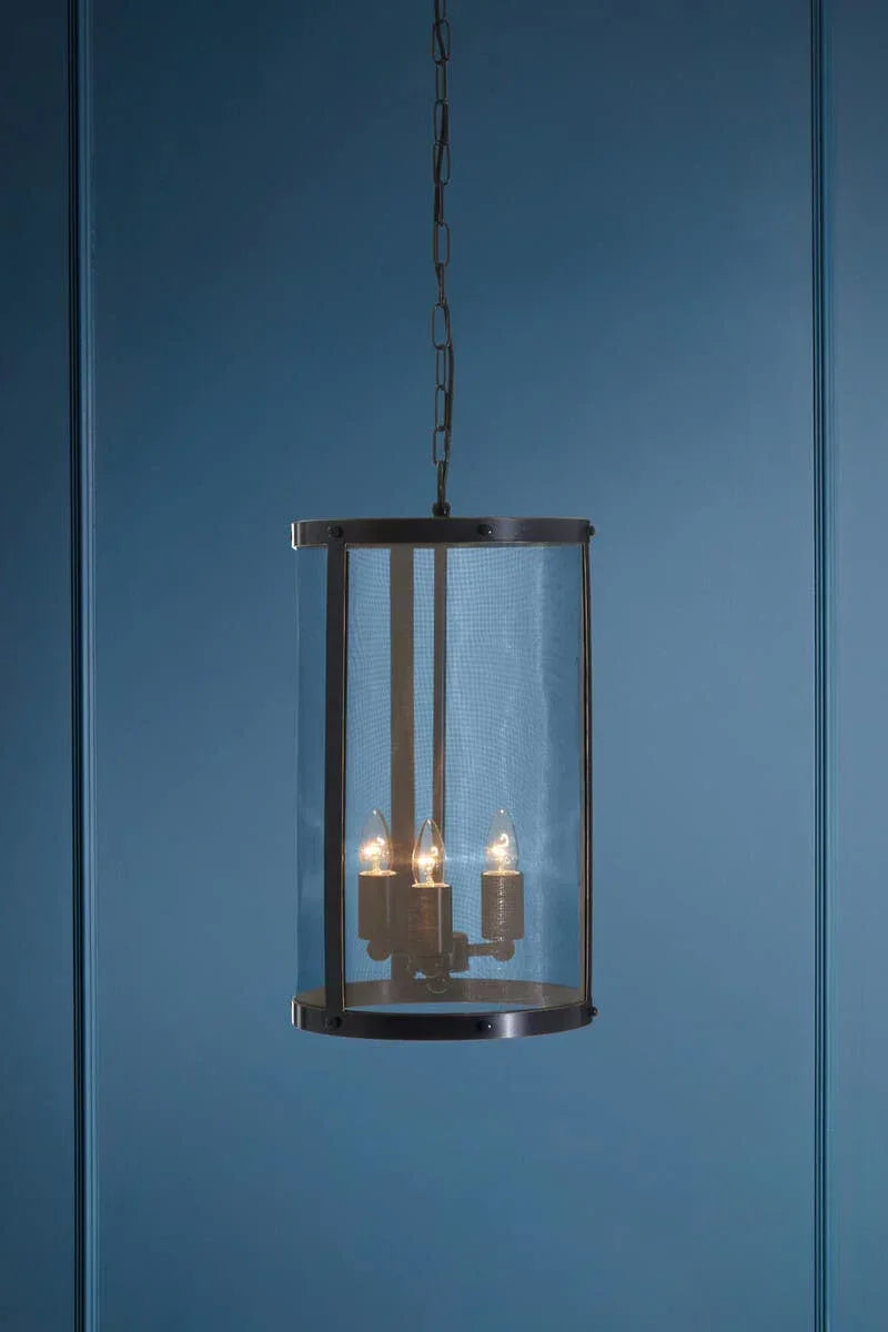 Black metal pendant light with mesh shade and three bulbs against blue wall