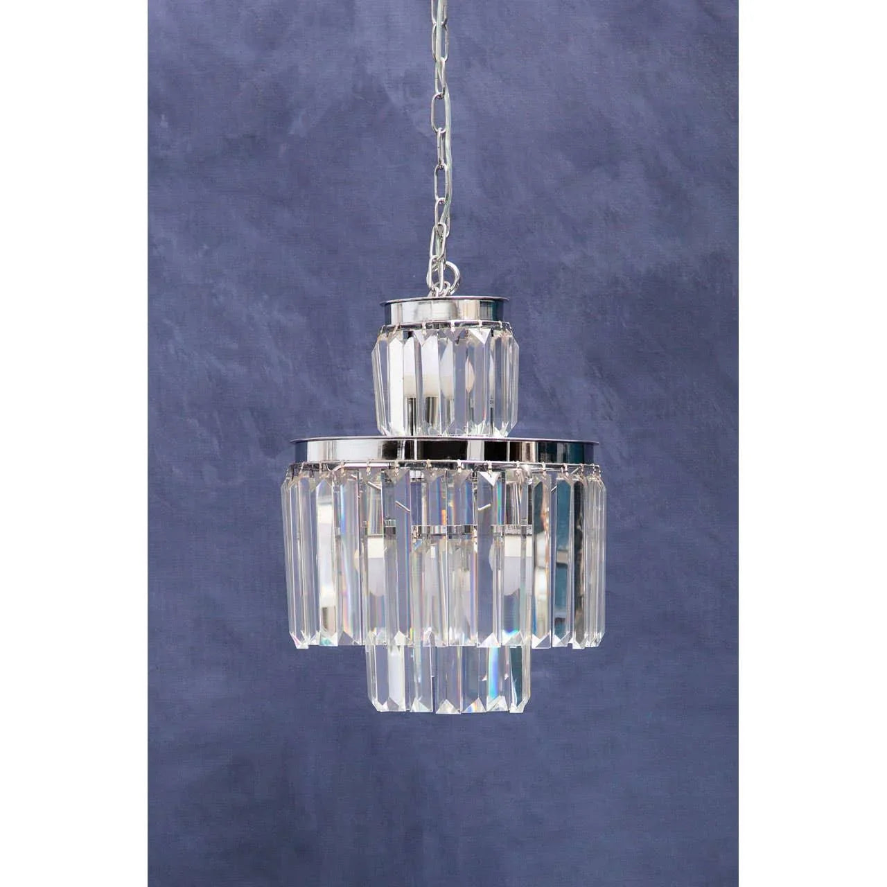 Tiered crystal chandelier with chrome accents hanging against a matte blue background