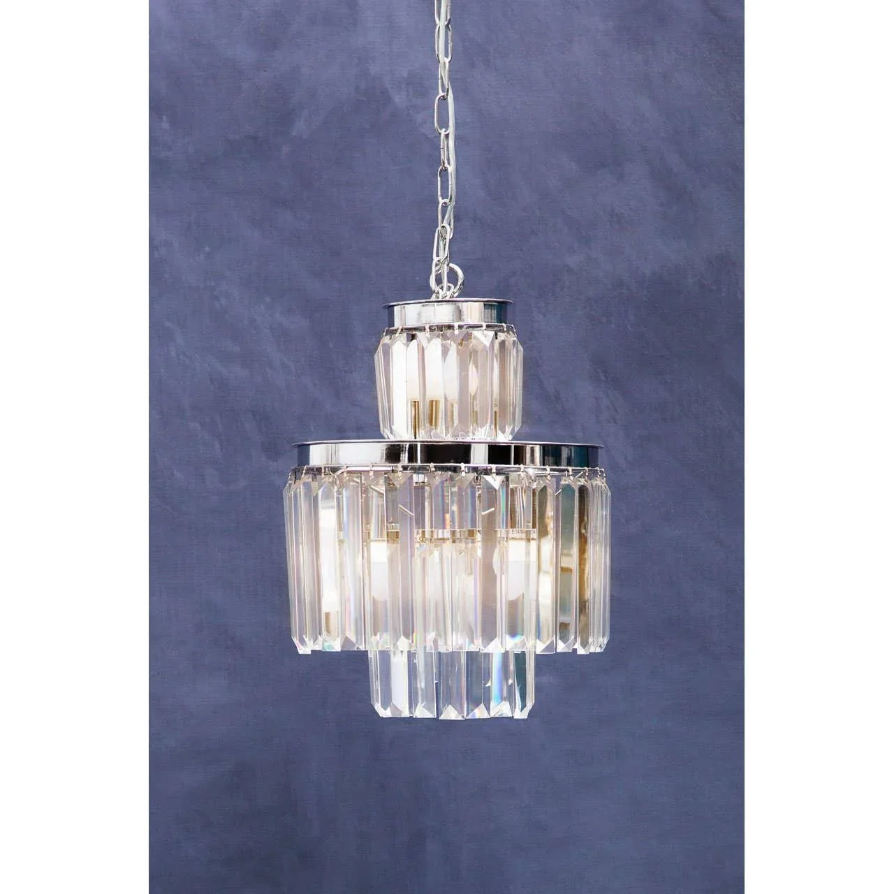 Crystal tiered chandelier with chrome finish suspended against a blue wall