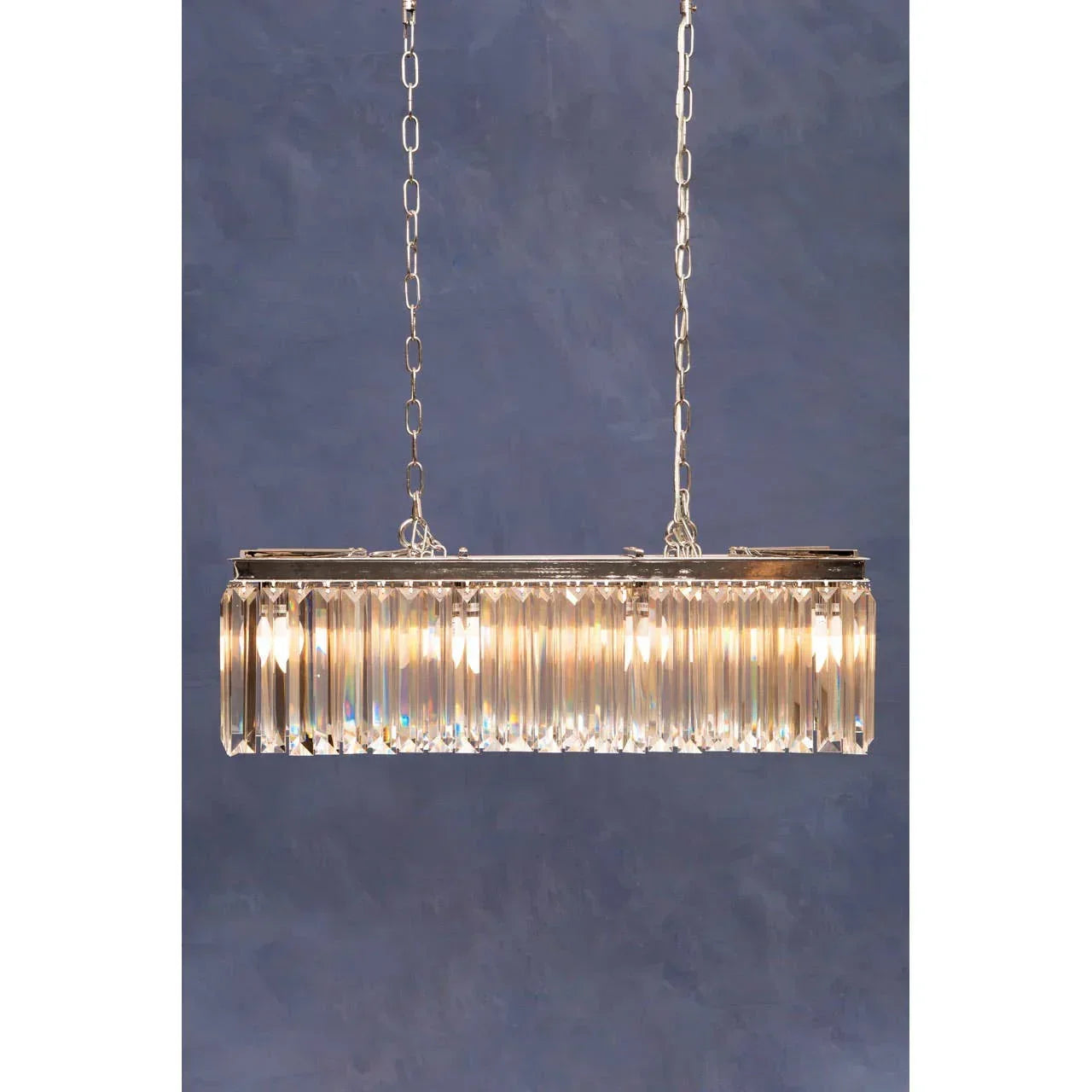 Rectangular crystal chandelier with chrome finish and warm lighting on blue background