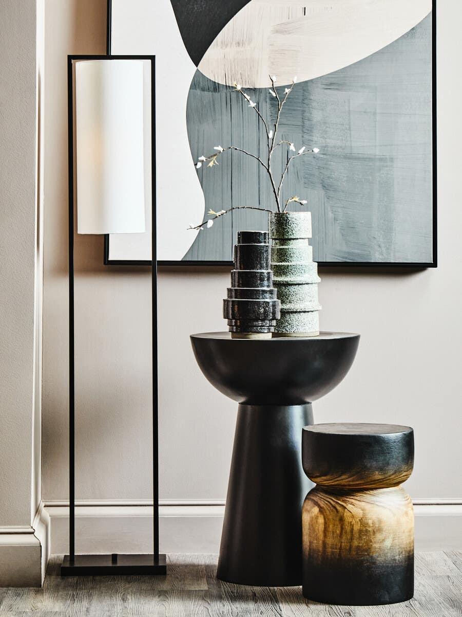 Modern floor lamp with white shade beside black side table, decorative vases, and stool