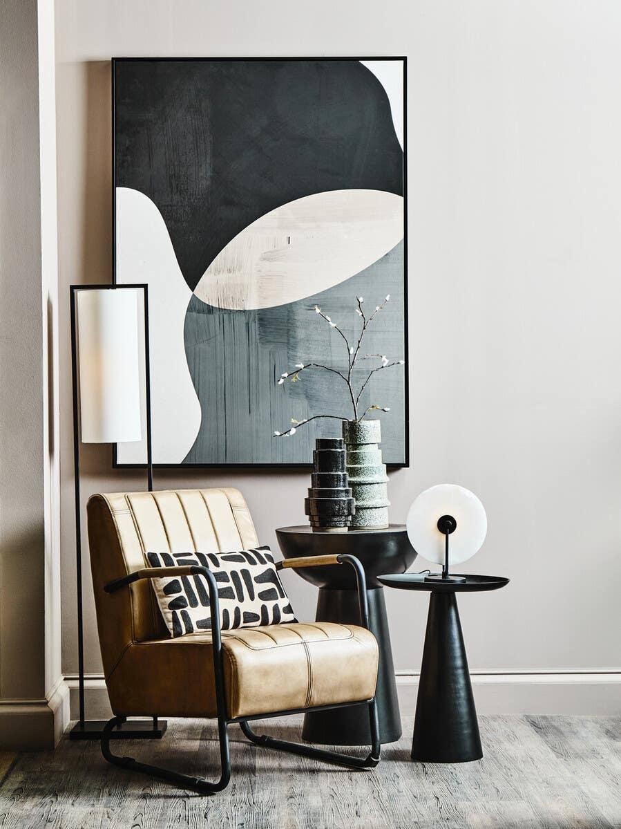 Tan leather accent chair with black frame, geometric pillow, and side tables in modern living room