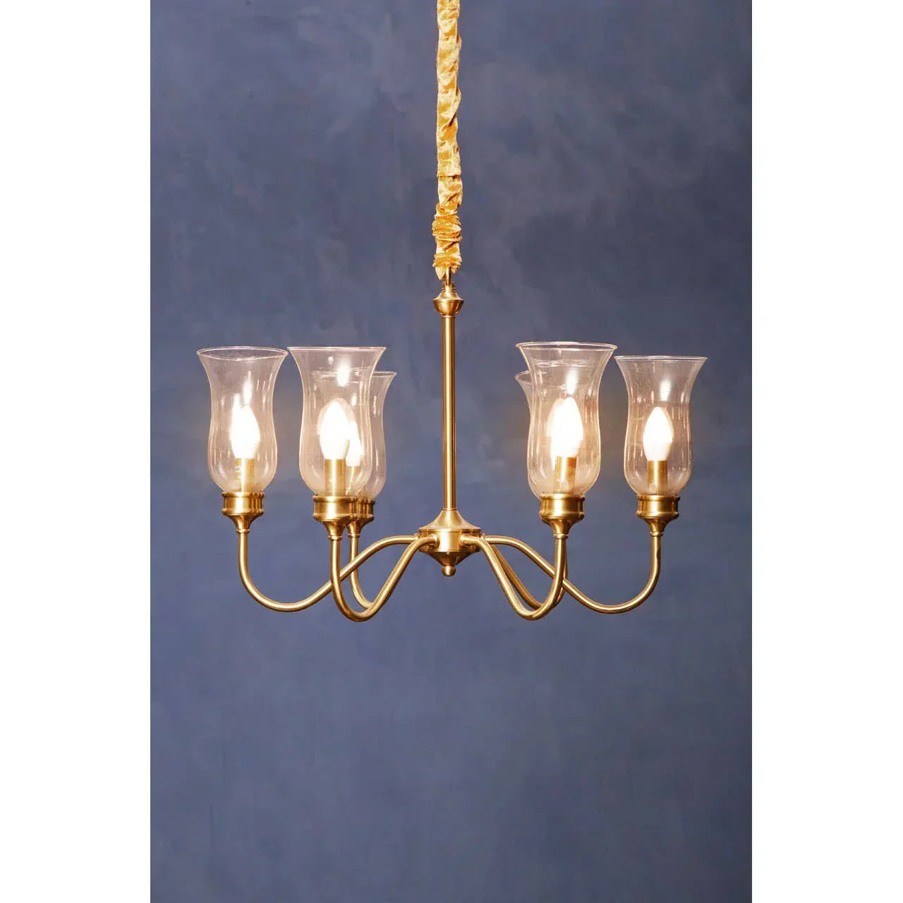 Brass chandelier with four glass lamp shades and exposed bulbs against blue background
