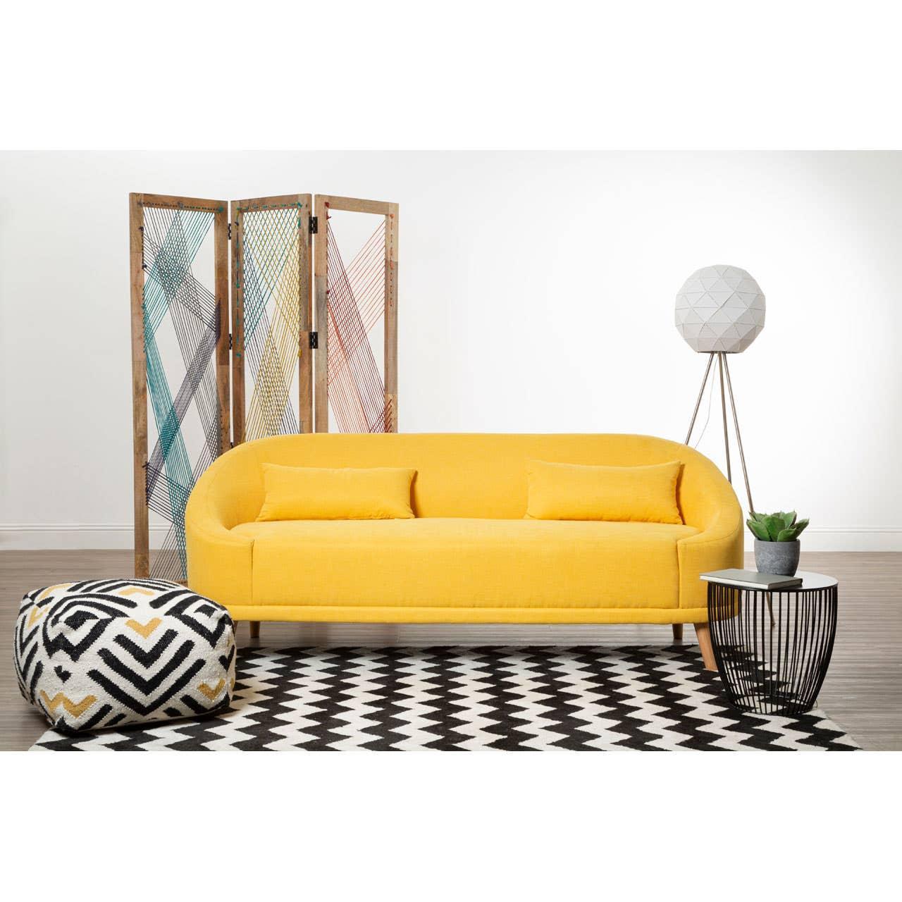 Yellow fabric sofa with two cushions, patterned pouffe, and side table on black and white rug