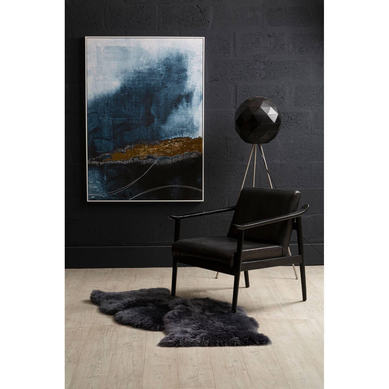 Black leather accent chair with wooden arms beside abstract painting and tripod floor lamp