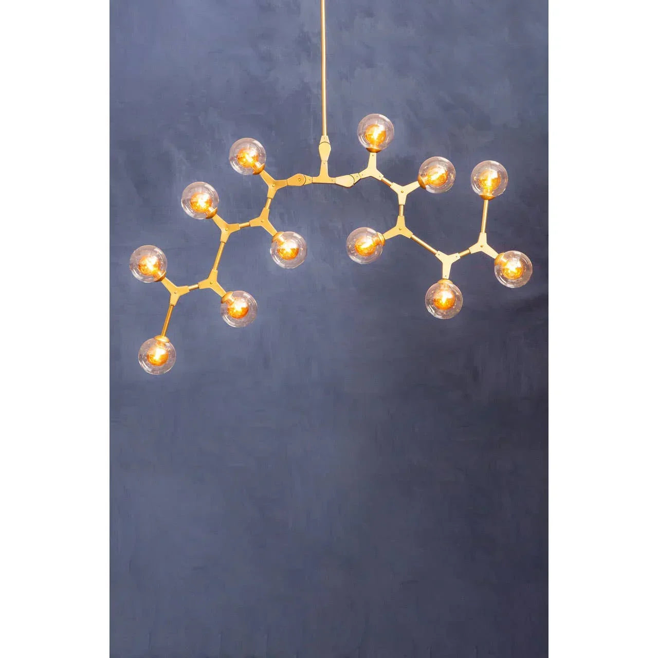 Gold modern chandelier with 14 glass globe bulbs against a dark blue wall