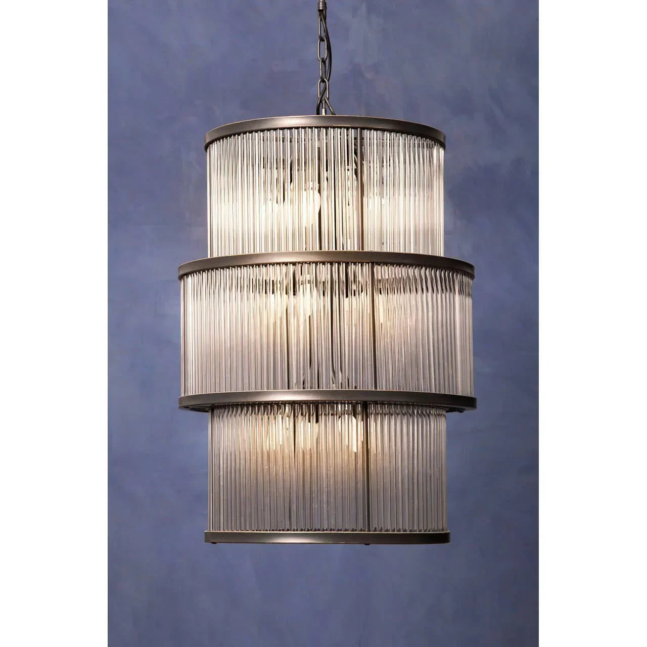 Three tier glass rod chandelier with metal frame hanging against blue wall