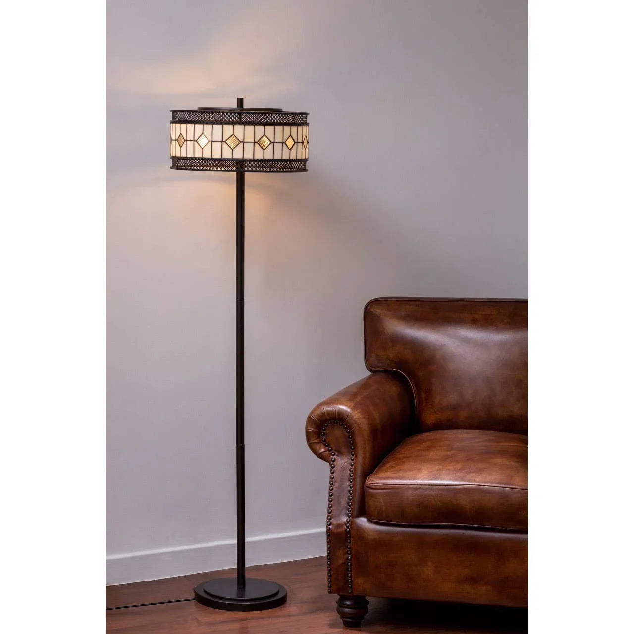 Brown leather sofa beside tall stained glass floor lamp against neutral wall