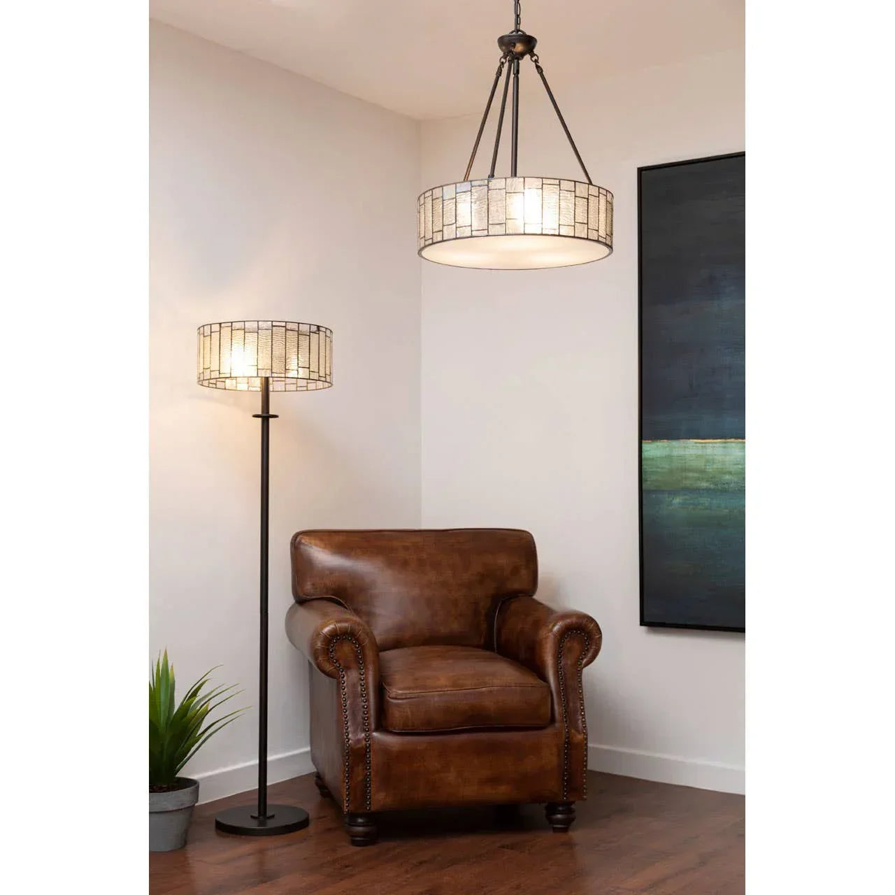 Brown leather armchair with studded arms beside floor lamp and modern wall art