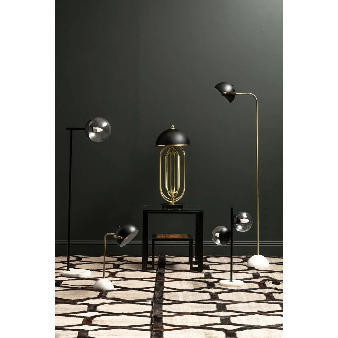 Modern black and gold table and floor lamps on patterned rug against dark wall