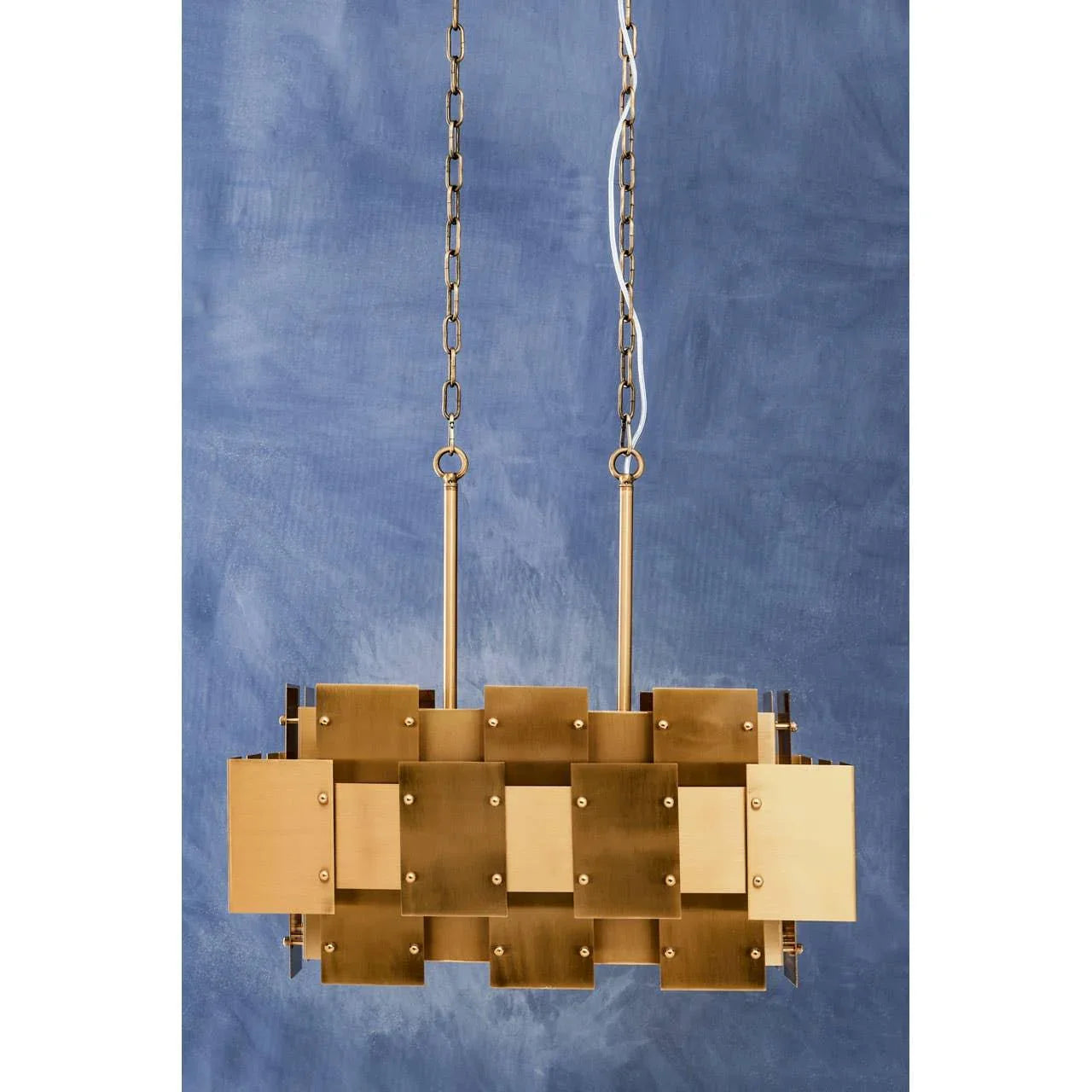 Brass geometric pendant light with rectangular panels on gold chains against blue wall