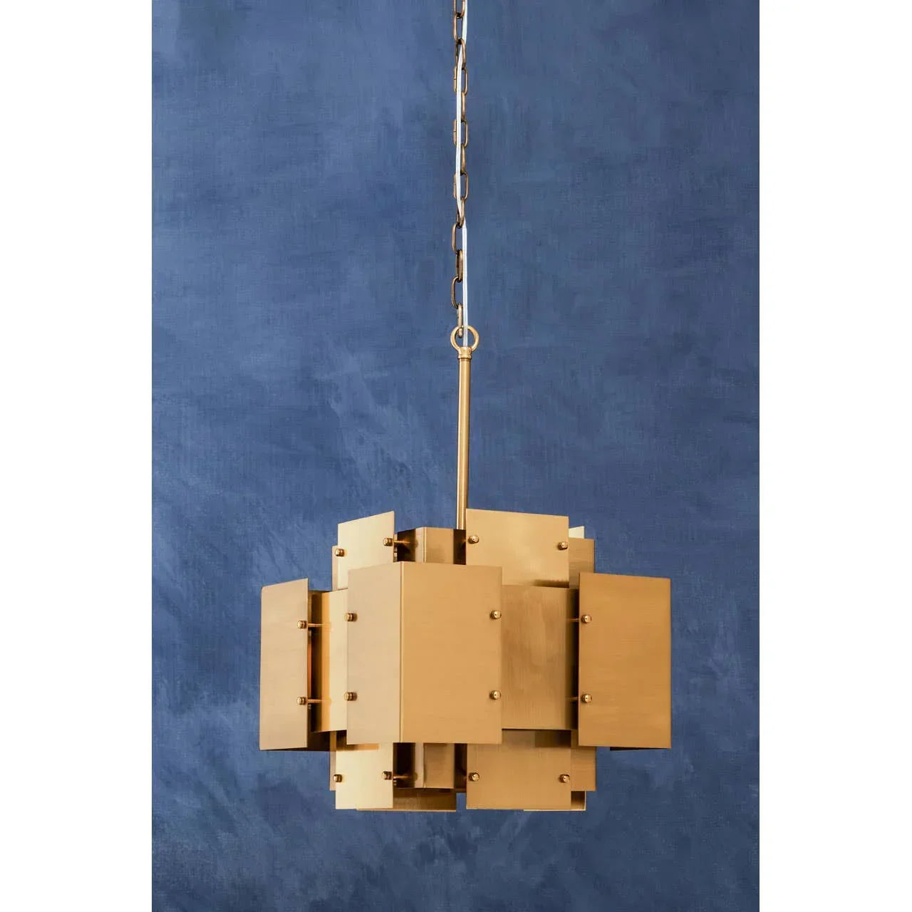 Modern gold pendant light with geometric metal panels against a blue wall