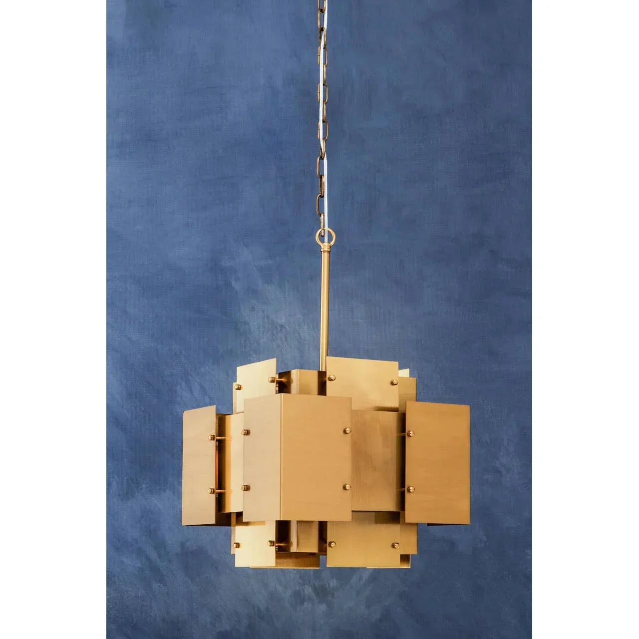 Modern gold pendant light with geometric panels and chain against blue wall