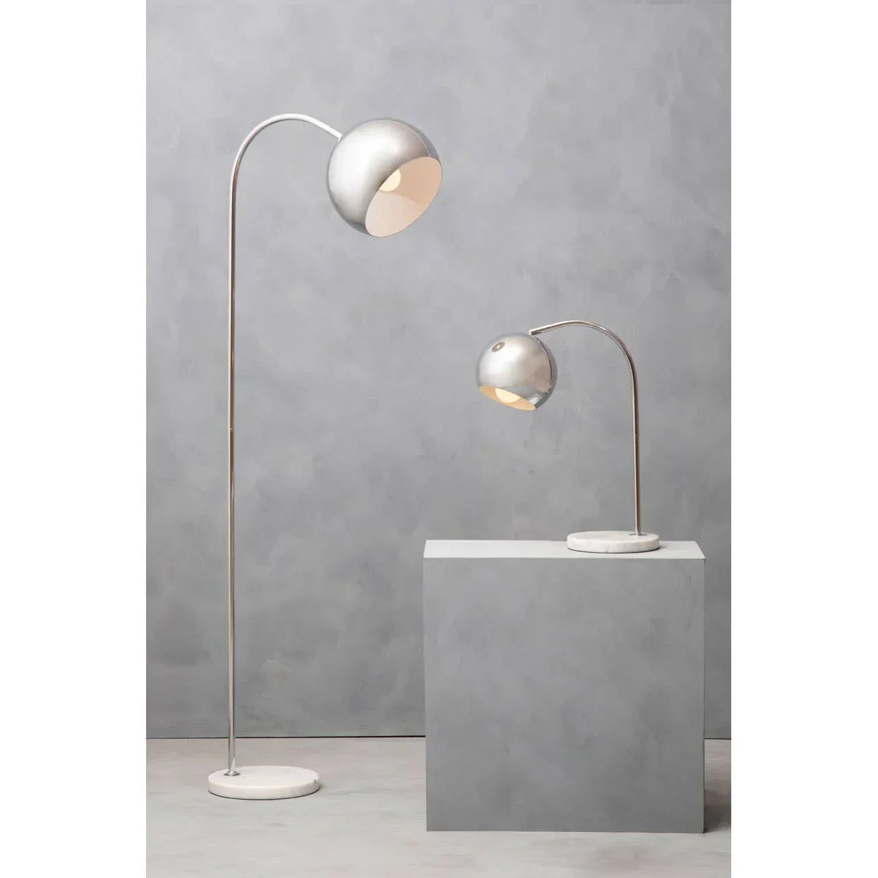 Modern silver floor lamp and matching table lamp with marble bases against grey background