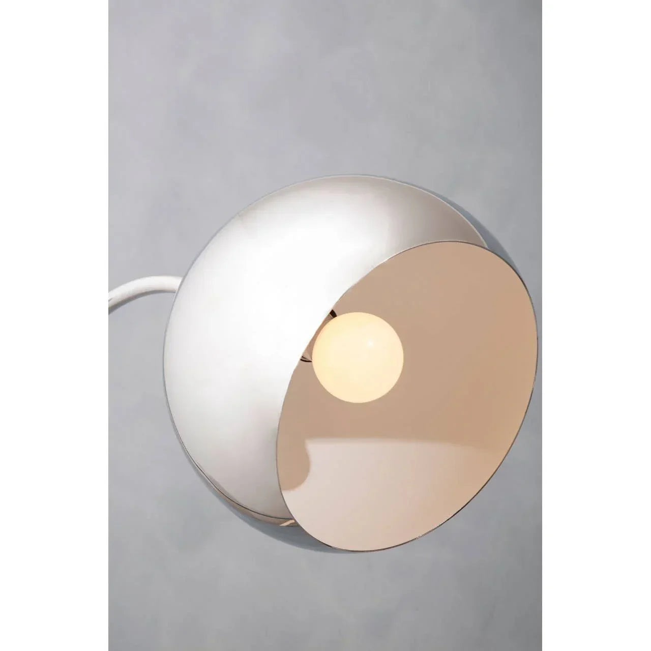 Modern white metal wall lamp with round shade and exposed bulb against grey background