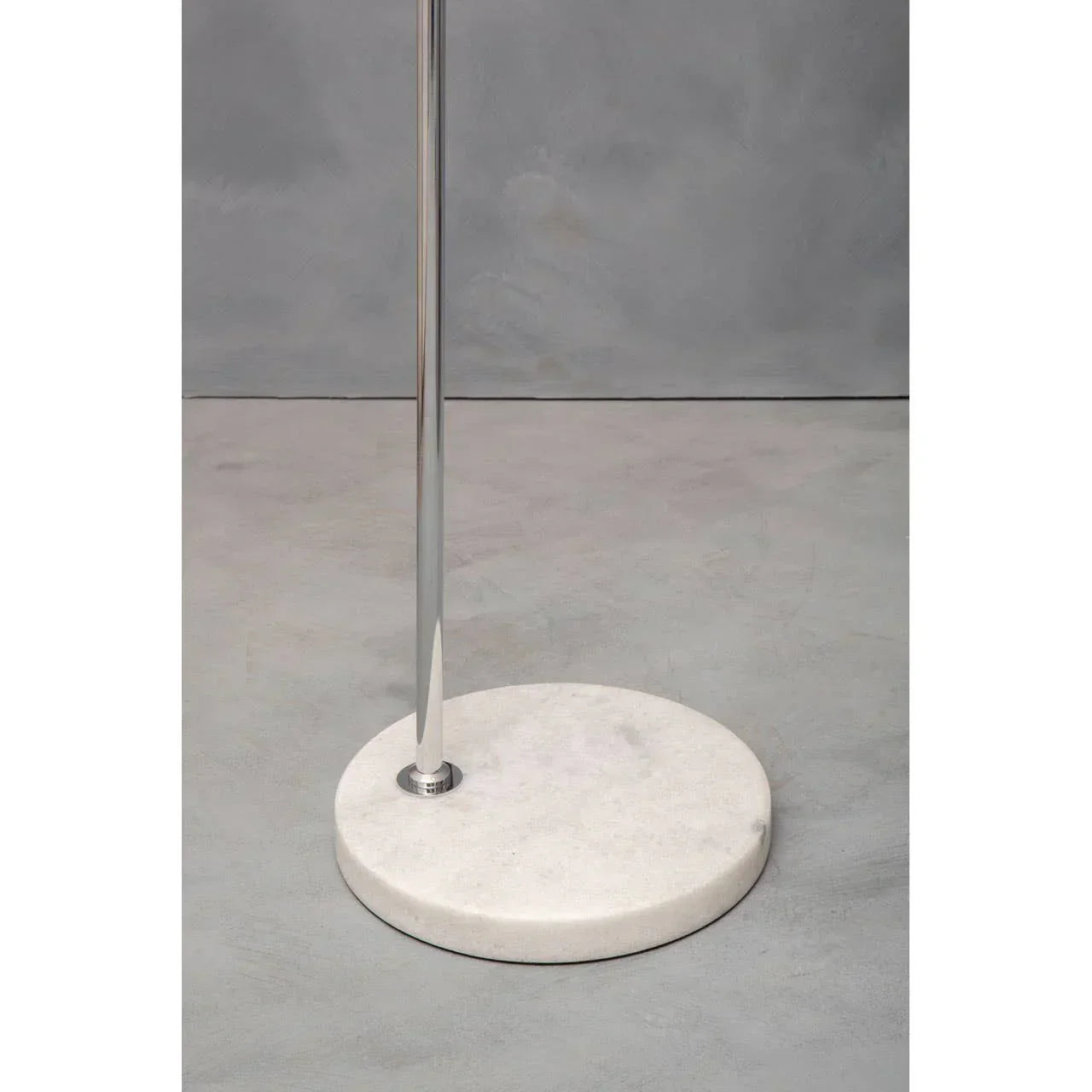 Modern floor lamp with chrome pole and round white marble base on grey floor