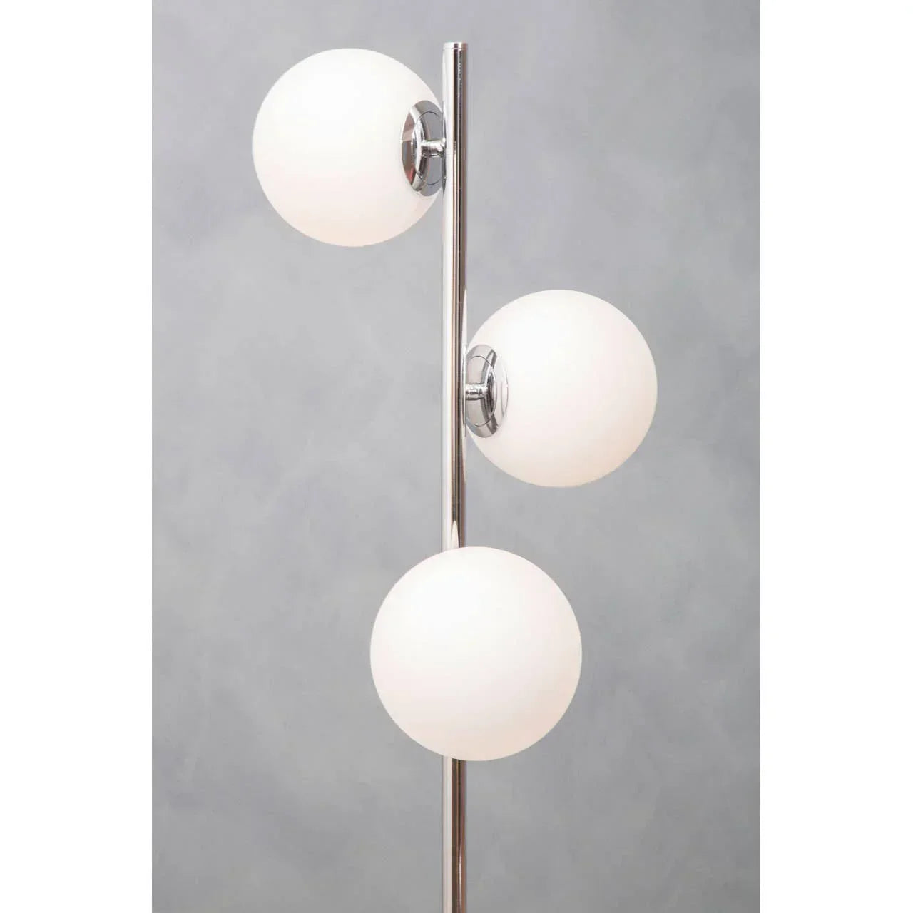 Chrome floor lamp with three round white glass shades against grey background