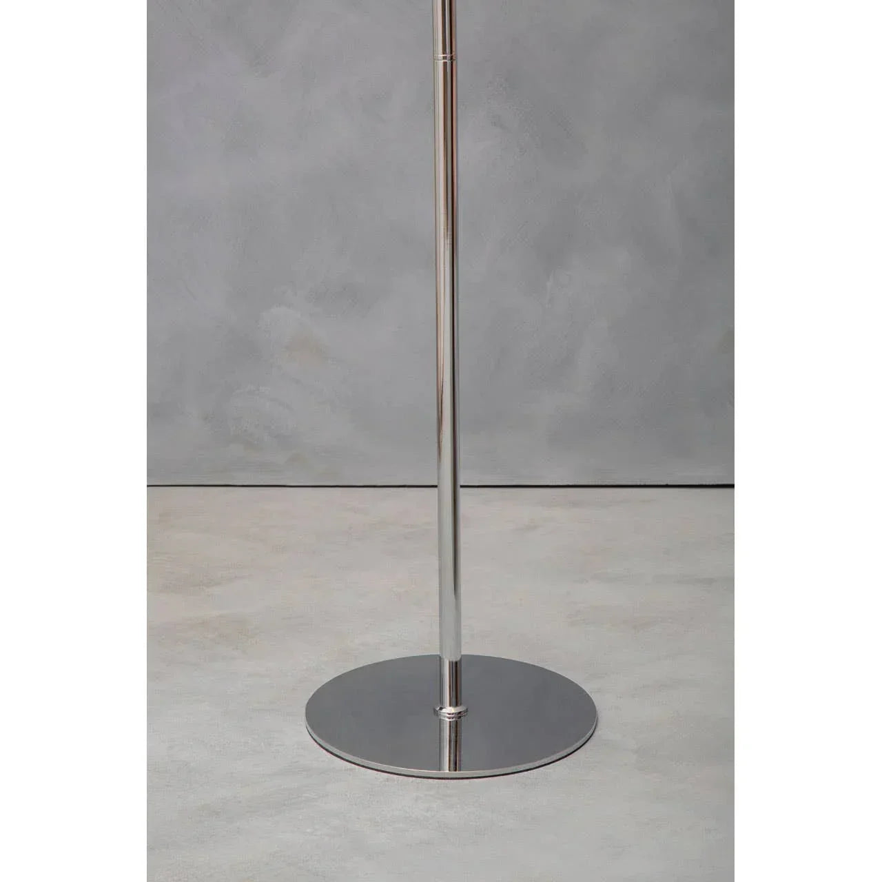 Chrome metal floor lamp base with round disc on light grey surface