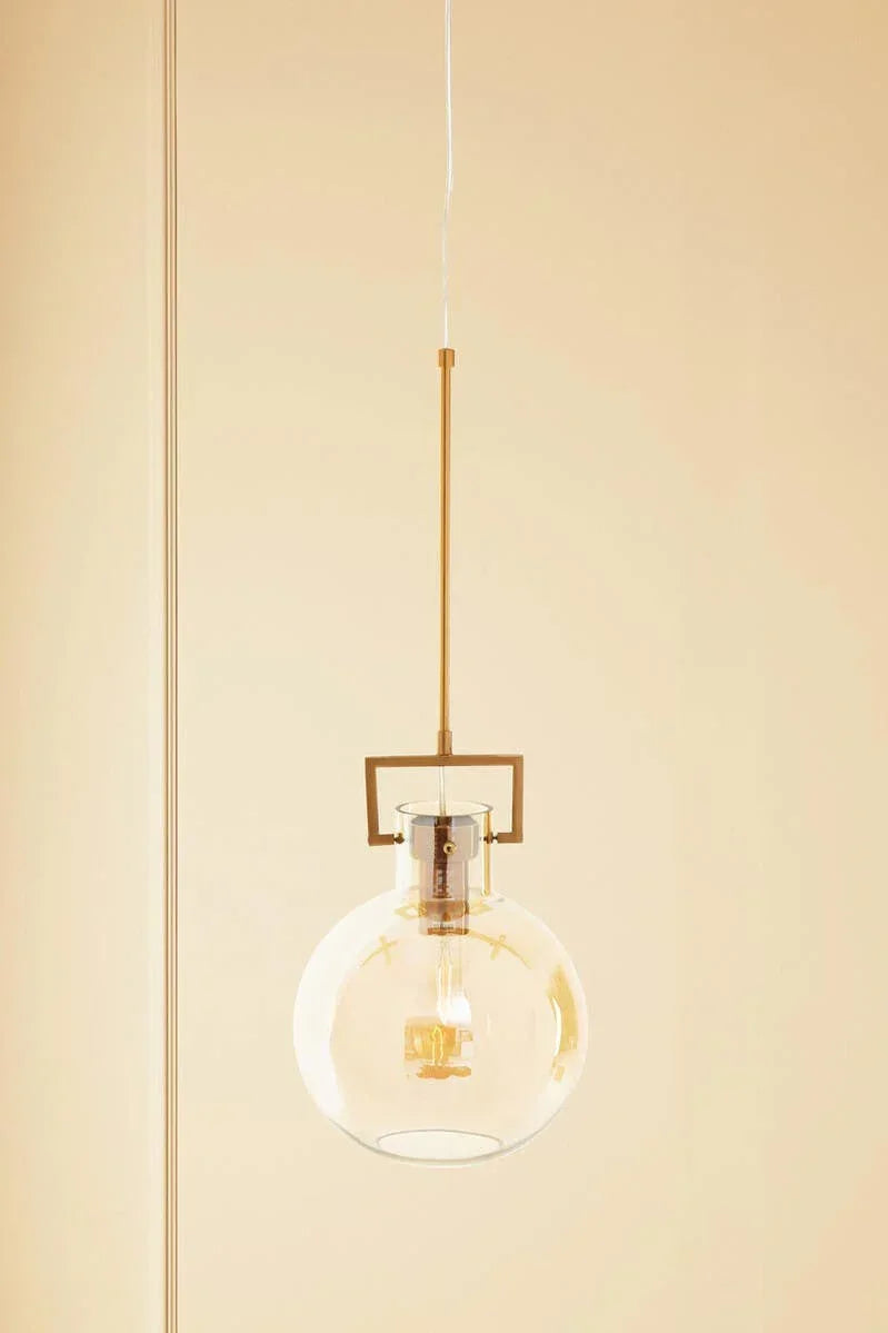 Glass globe pendant light with gold metal rod and exposed bulb against neutral wall