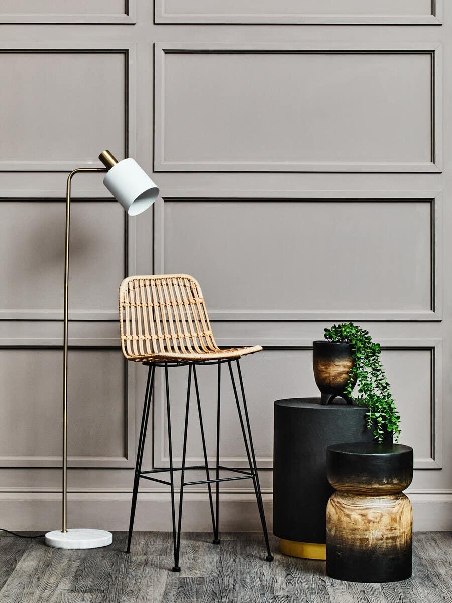 Rattan bar stool with metal legs beside modern side tables and indoor floor lamp