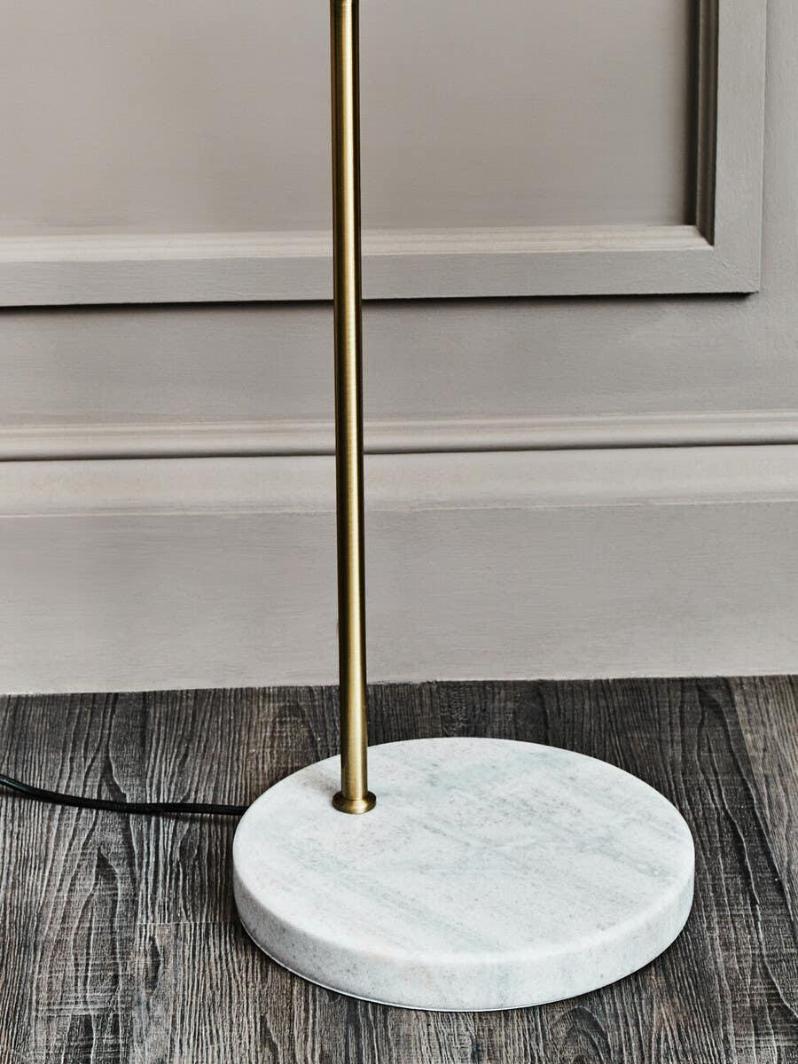 Brass floor lamp with white marble base on dark wood flooring