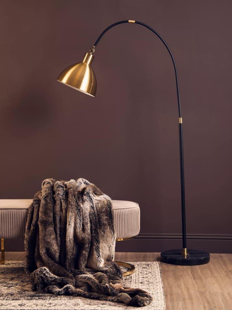 Gold floor lamp with black curved stand beside beige bench and faux fur throw on rug
