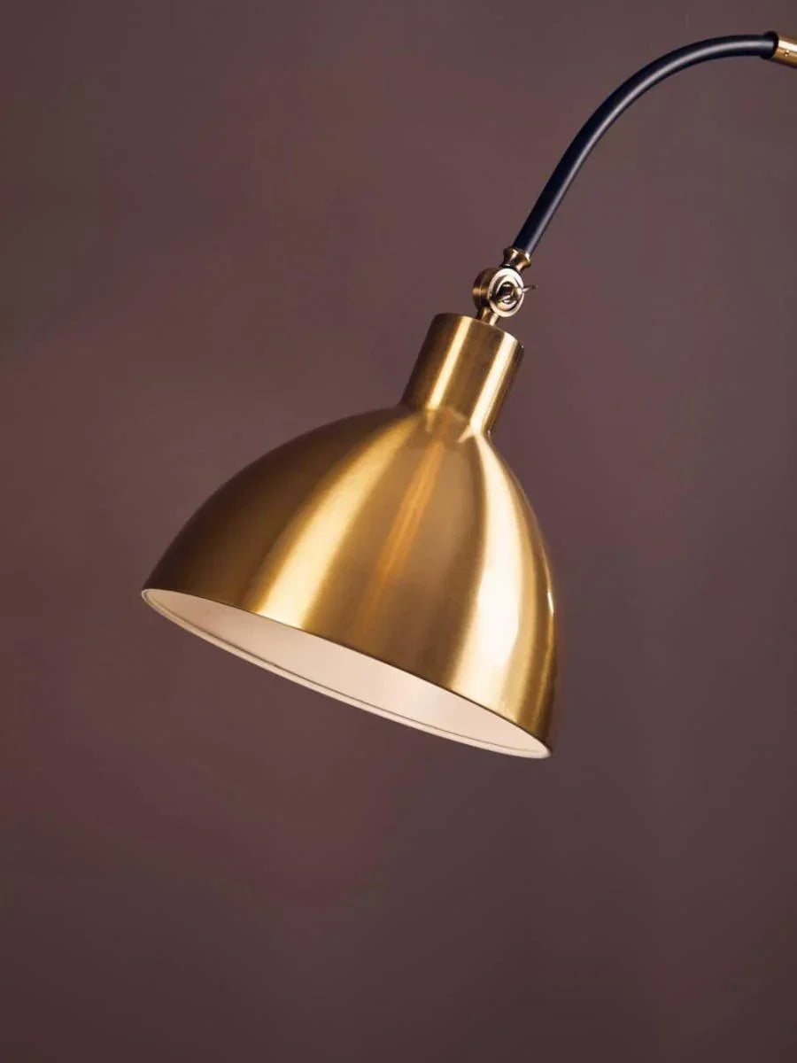 Brass metal arc floor lamp with curved black arm against a brown background