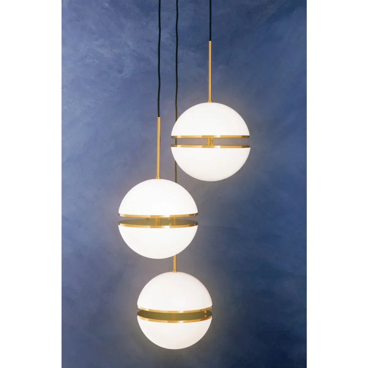 Modern pendant light with three white glass globes and gold trim on blue background